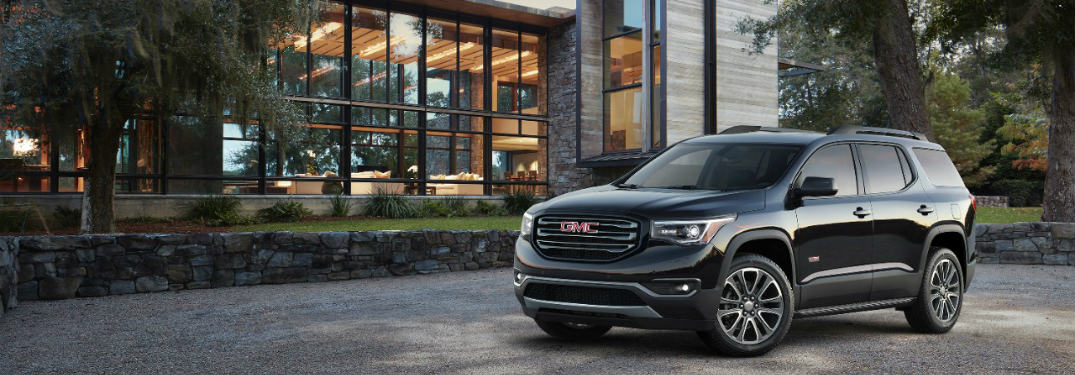 black 2017 GMC Acadia midsize SUV parked in front of a building with a big glass window