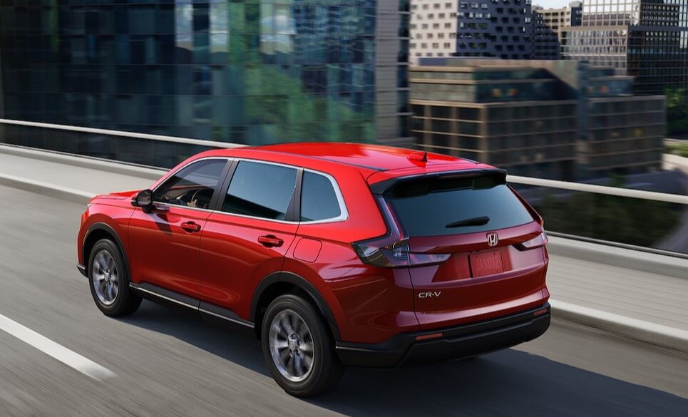 A new, red 2025 Honda CR-V drives on an open city road, making this a perfect midsize SUV for your work commute in Columbia. 