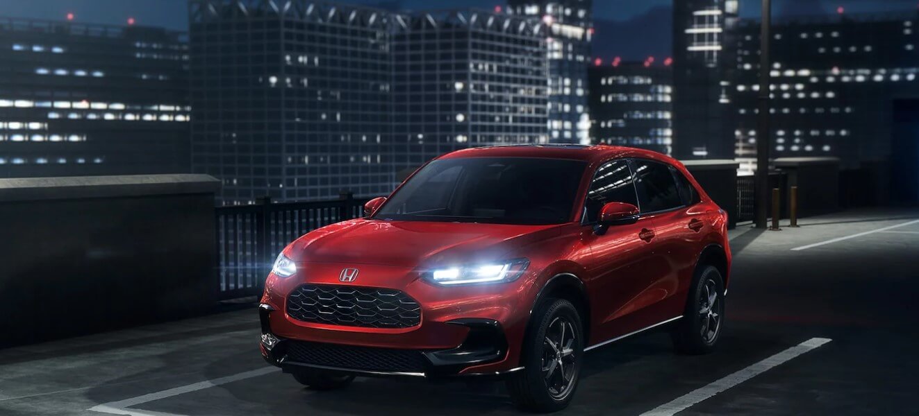 A red 2025 Honda HR-V with its headlights on at night, showcasing it's sleek style on a city road. Shop for your new 2025 Honda HR-V at Midlands Honda near Columbia today.
