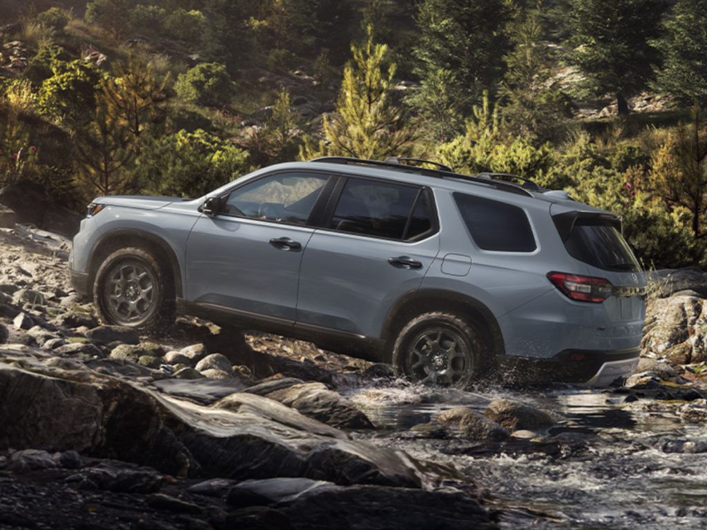 A grey 2025 Honda Pilot drives through a rocky riverbed.