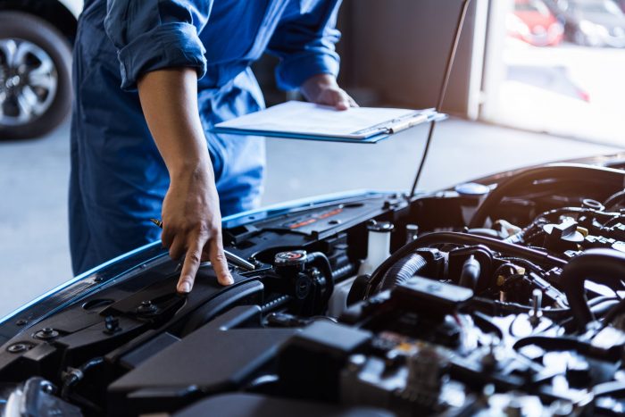 Car mechanic holding clipboard and checking to maintenance vehicle by customer claim order in auto repair shop garage. Engine repair service. People occupation and business job. Automobile technician