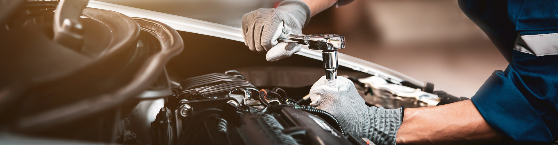 A mechanic wearing gray gloves uses a wrench to work on a car engine, focusing intently. The image conveys professionalism and precision.