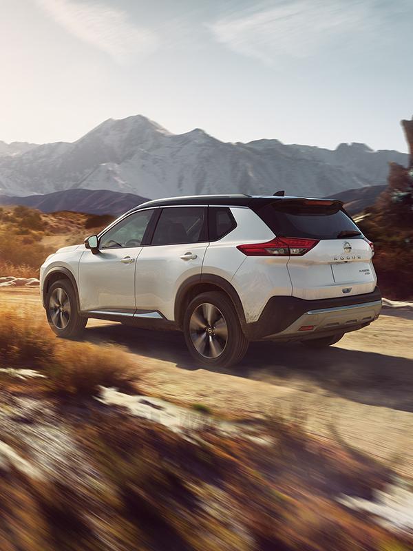 A white Nissan Rogue driving along a desert dirt road.