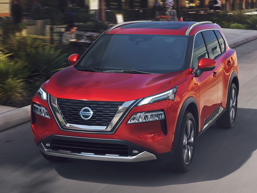 A red Nissan Rogue driving down a city street.