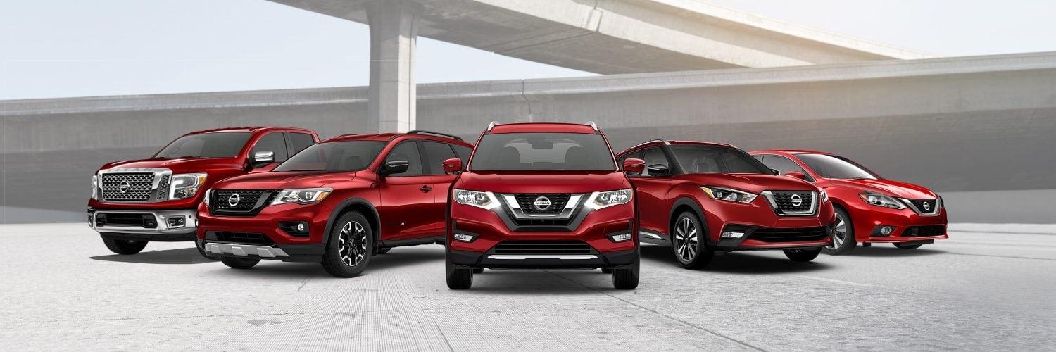 Lineup of Nissan vehicles in red with a highway overpass in the background.