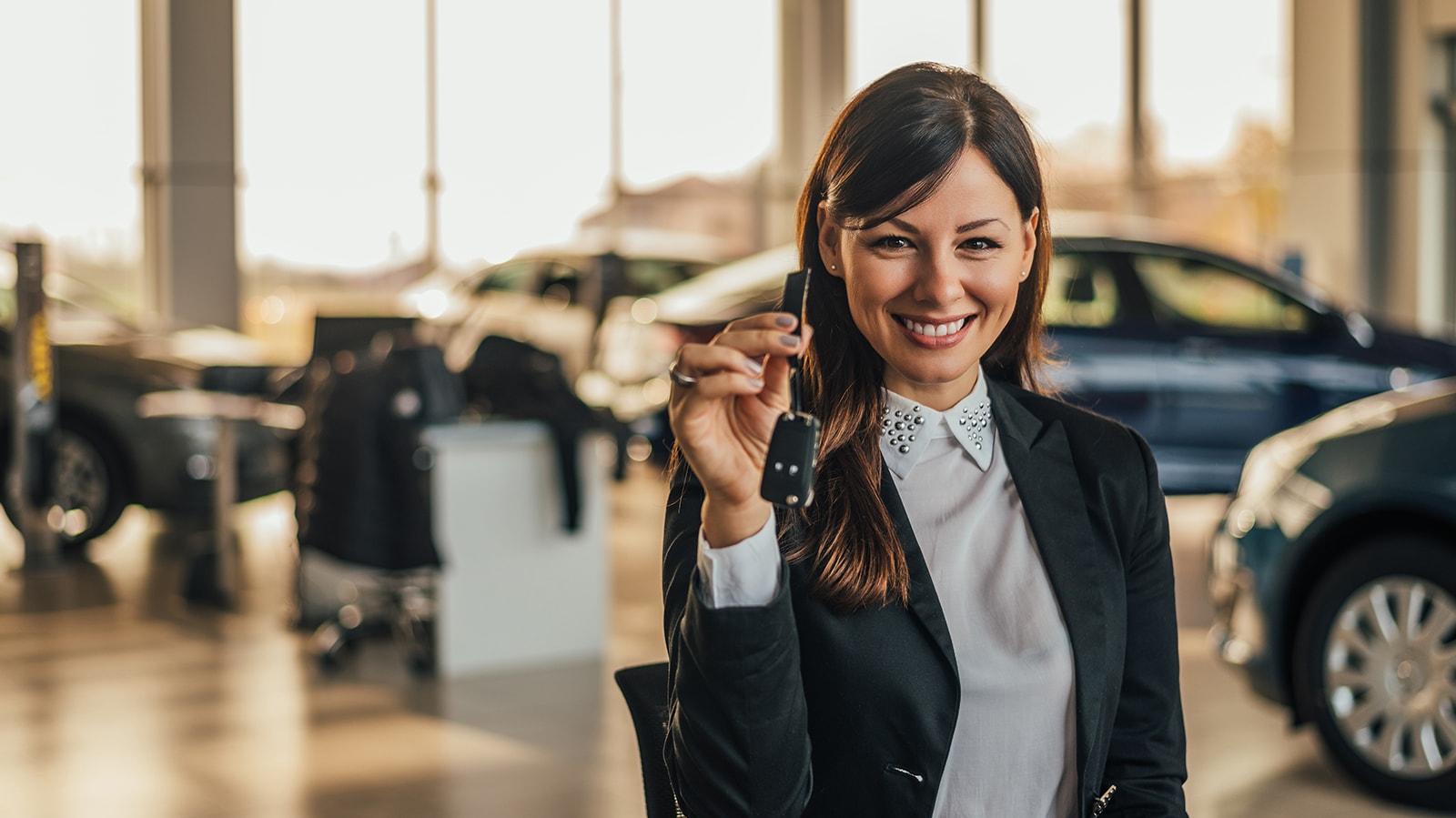 Smiling woman in a dealership holding new car keys