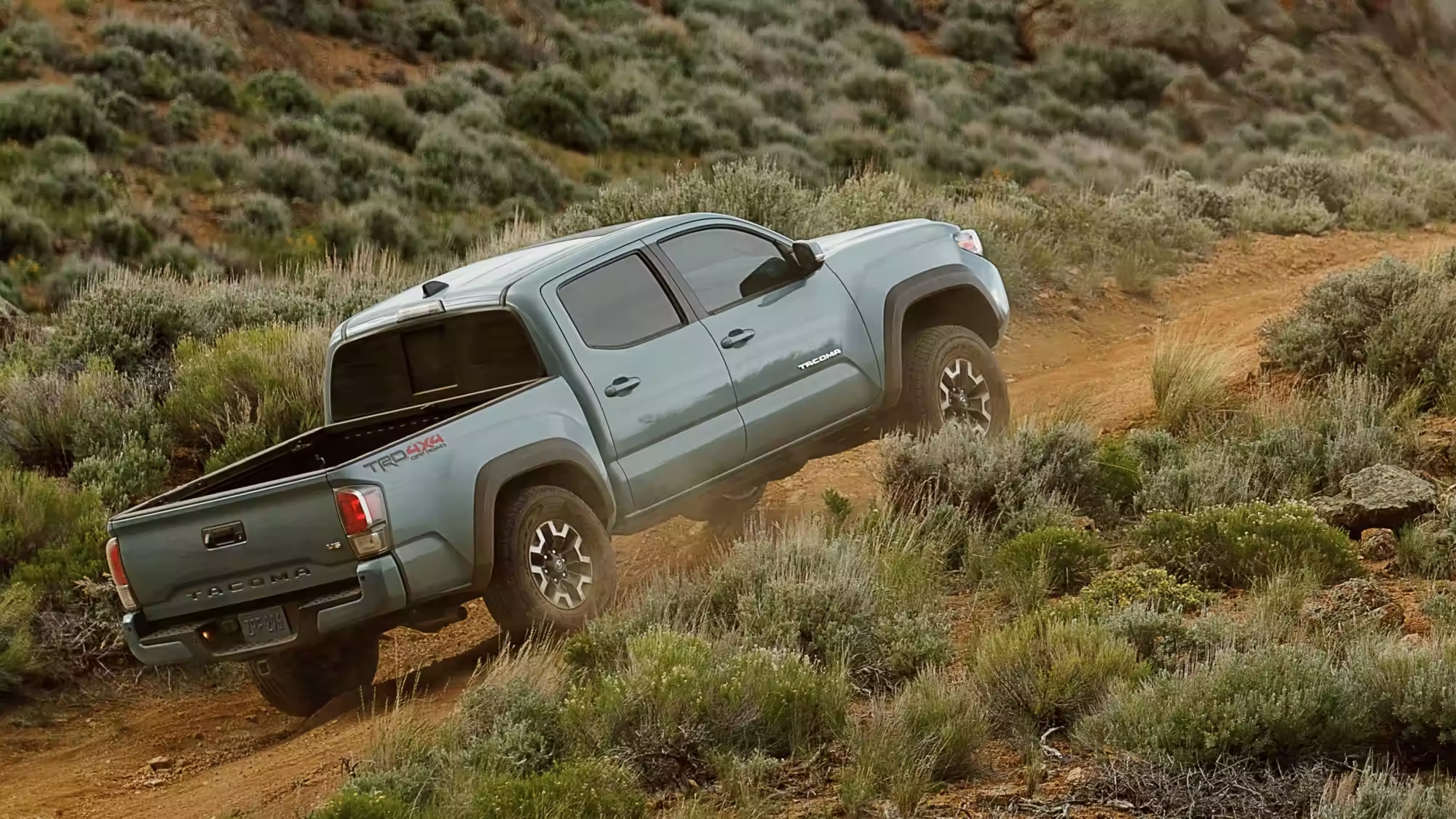 Grey 2023 Toyota Tacoma Driving up a hill in the desert on a dirt road