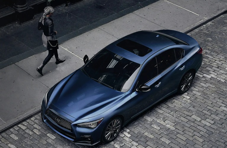 Woman walking by a blue INFINTI sedan