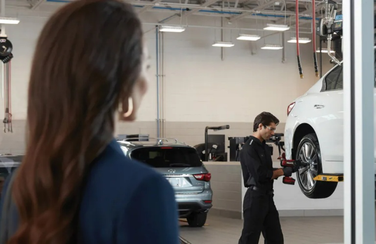 Woman looking on as a technician works on her INFINITI