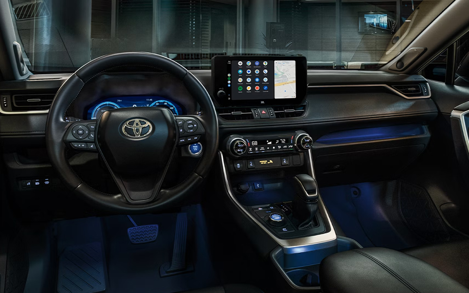 Interior of a Toyota RAV4 featuring a sleek, modern dashboard with a touchscreen displaying navigation. Blue ambient lighting enhances the premium design.