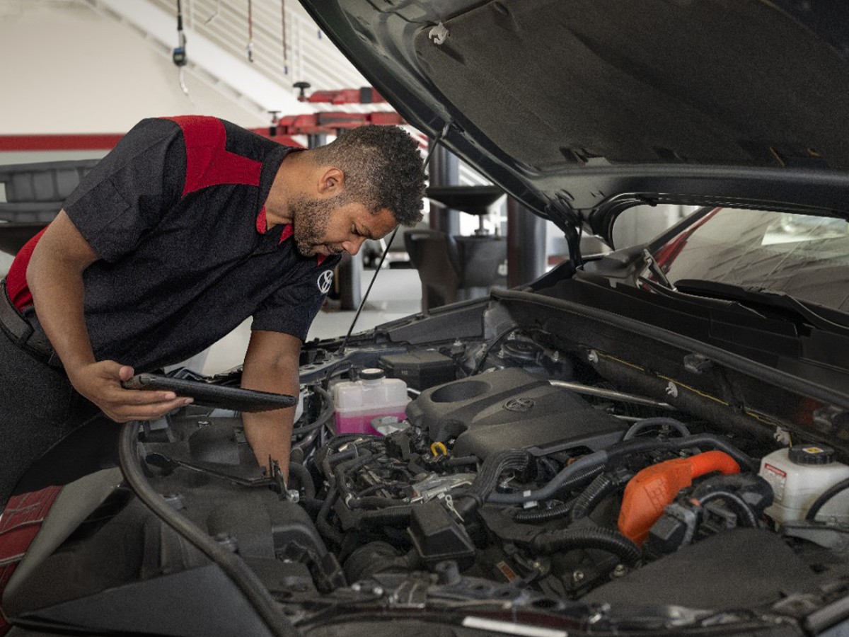 A toyota service technician leans over the engine of a car as he works his service magic.