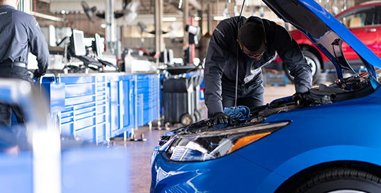 Mechanic working under hood of blue car