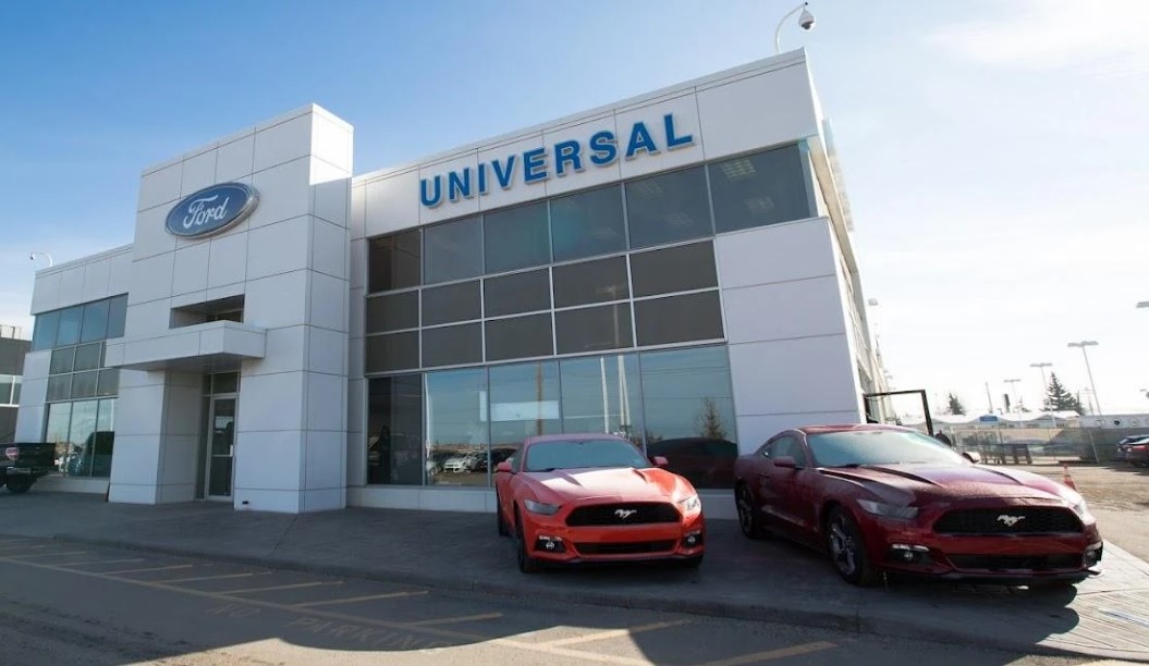 exterior look at Universal Ford’s dealership entrance with Ford Mustangs in the foreground on a summer morning