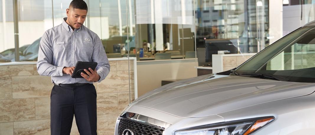 Putting out customers' health and comfort first. Image of INFINITI service associate taking notes on INFINITI vehicle.