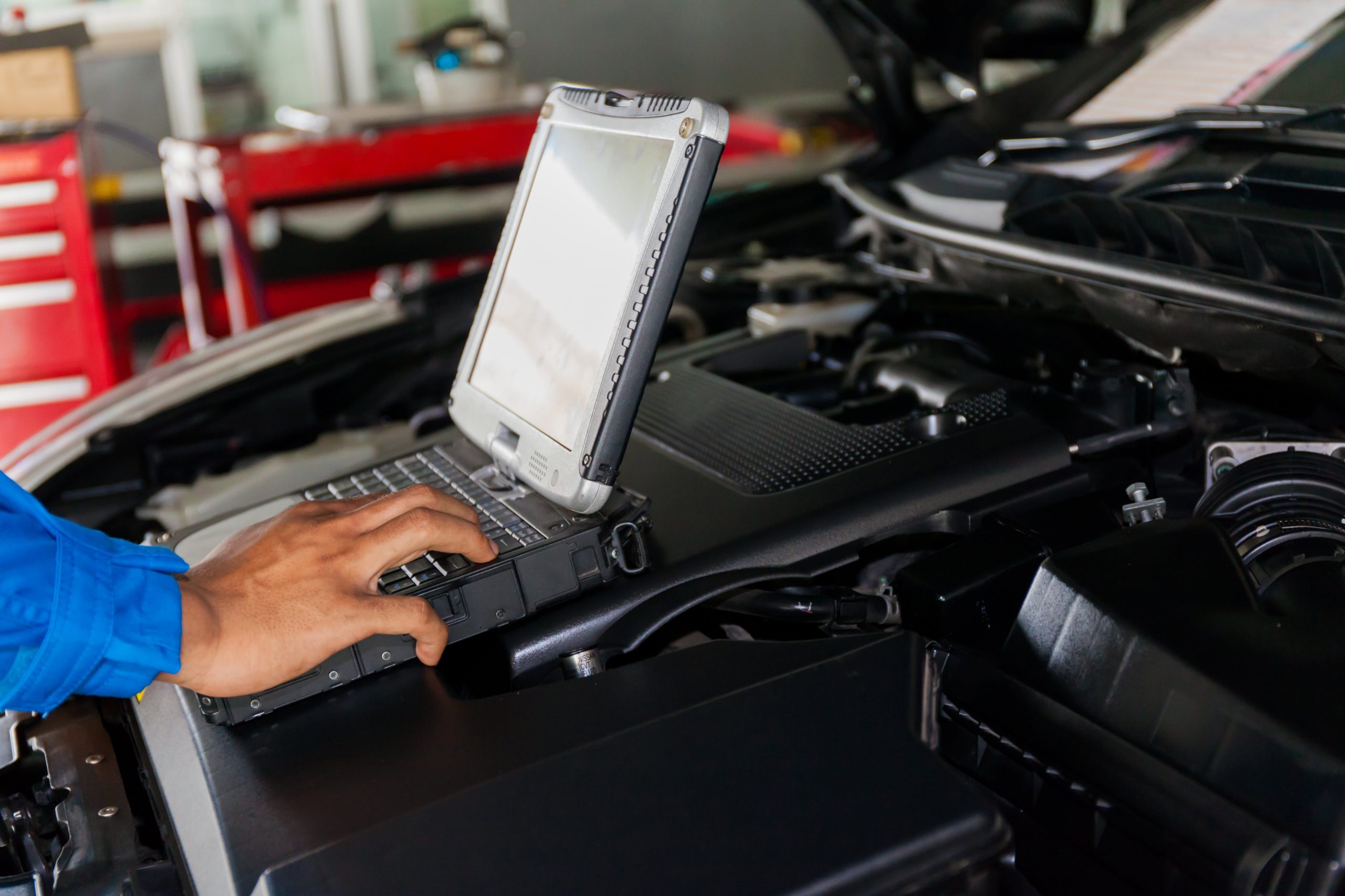 Mechanic inspecting a vehicle's engine with a laptop