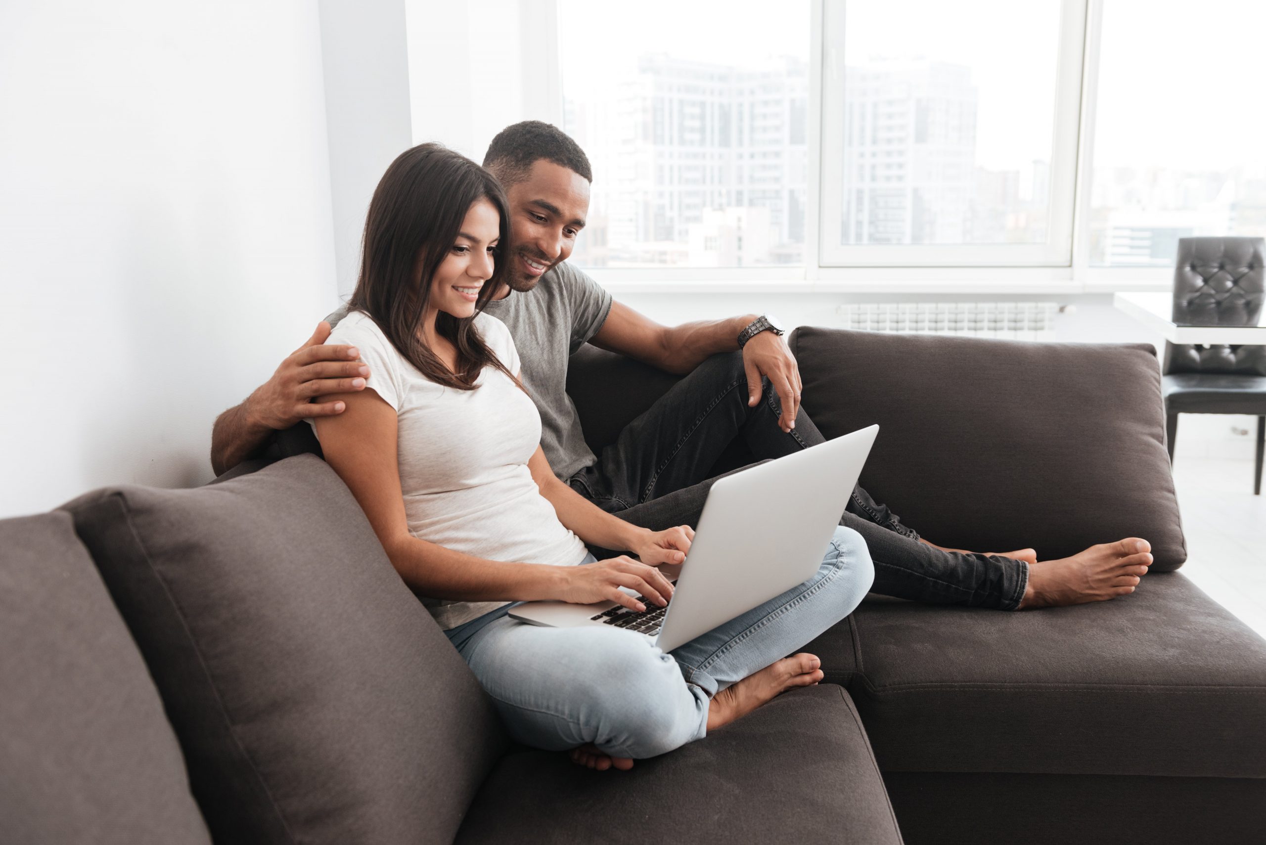 Young couple smiling and looking at a laptop while sitting on a couch