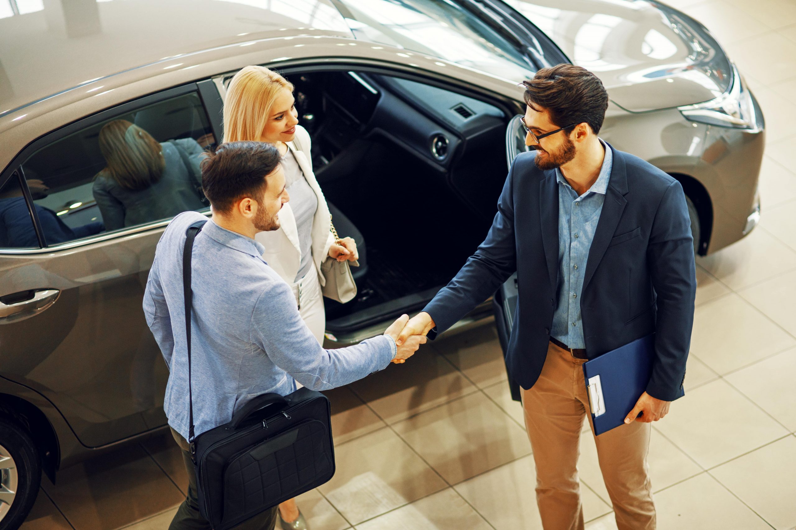 Couple shaking hands with a car salesman next to a car