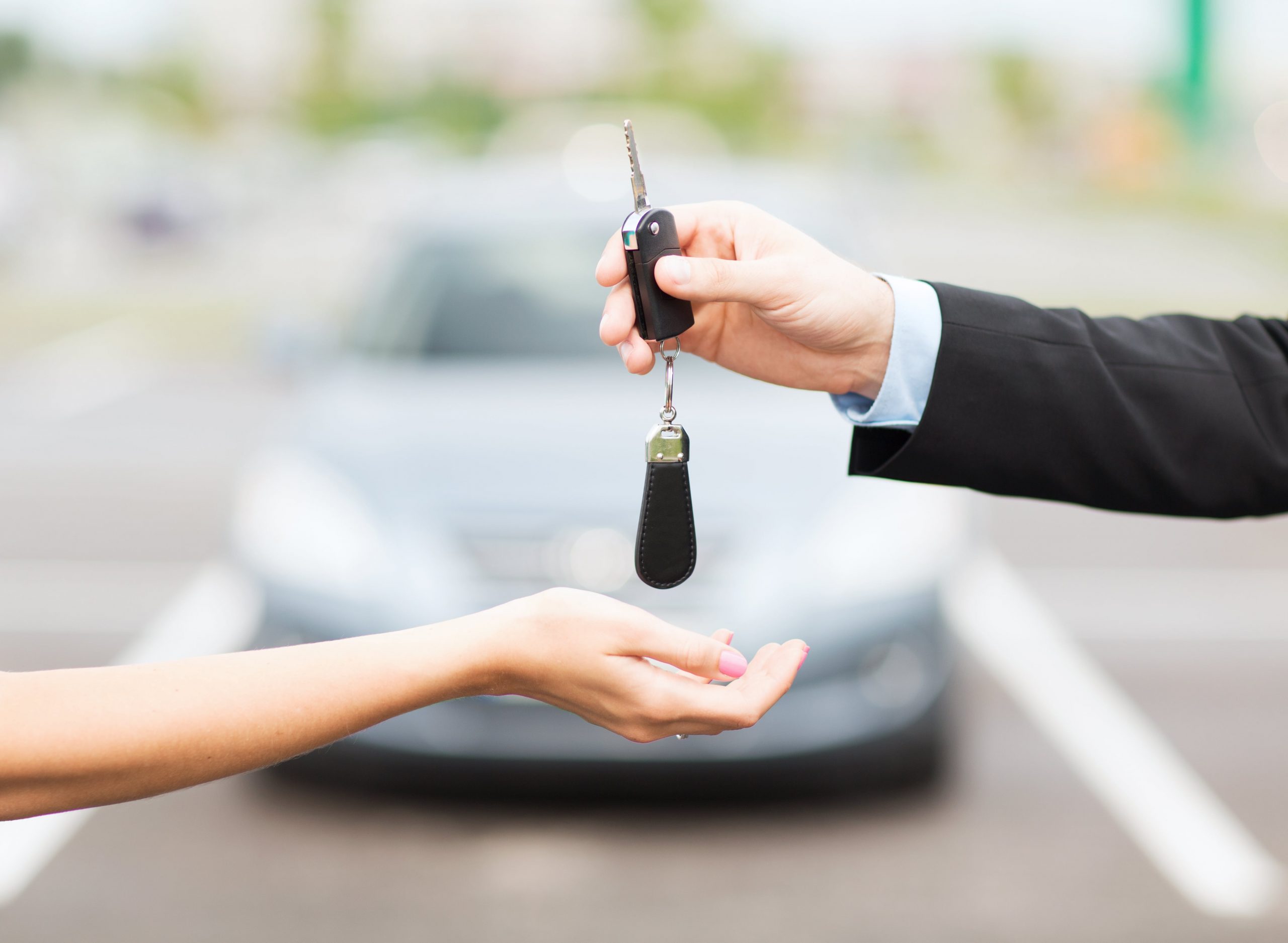Man handing a woman car keys with a blurred out car in the background