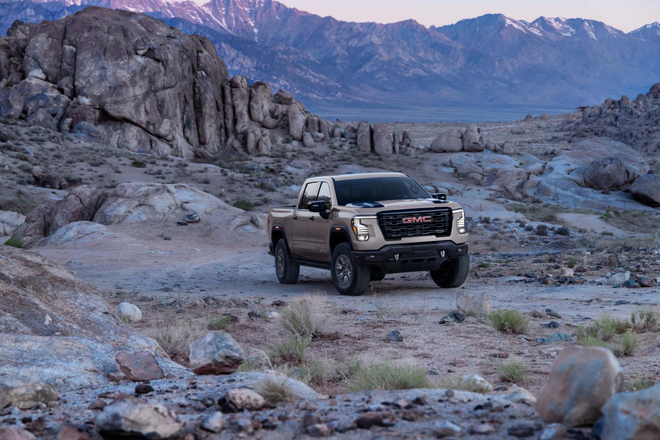 Close-up front view of a 2027 GMC Sierra 1500 grille and headlamps with a desert rock formation in the background