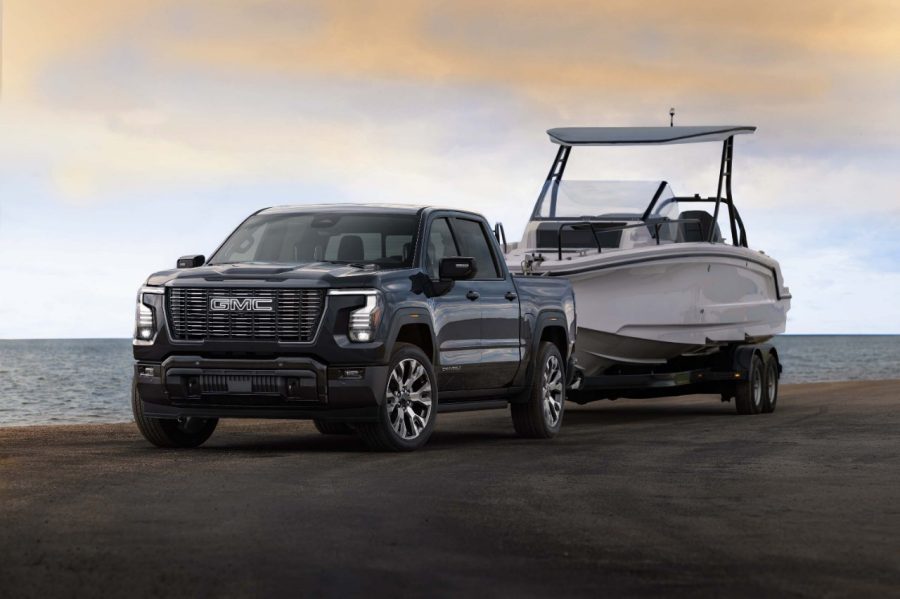Black 2027 GMC Sierra 1500 towing a large boat on a trailer near the water