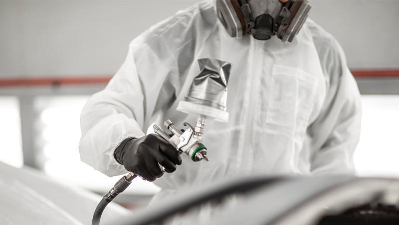 Painting technician applying paint to a car part at INFINITI of Las Vegas collision center